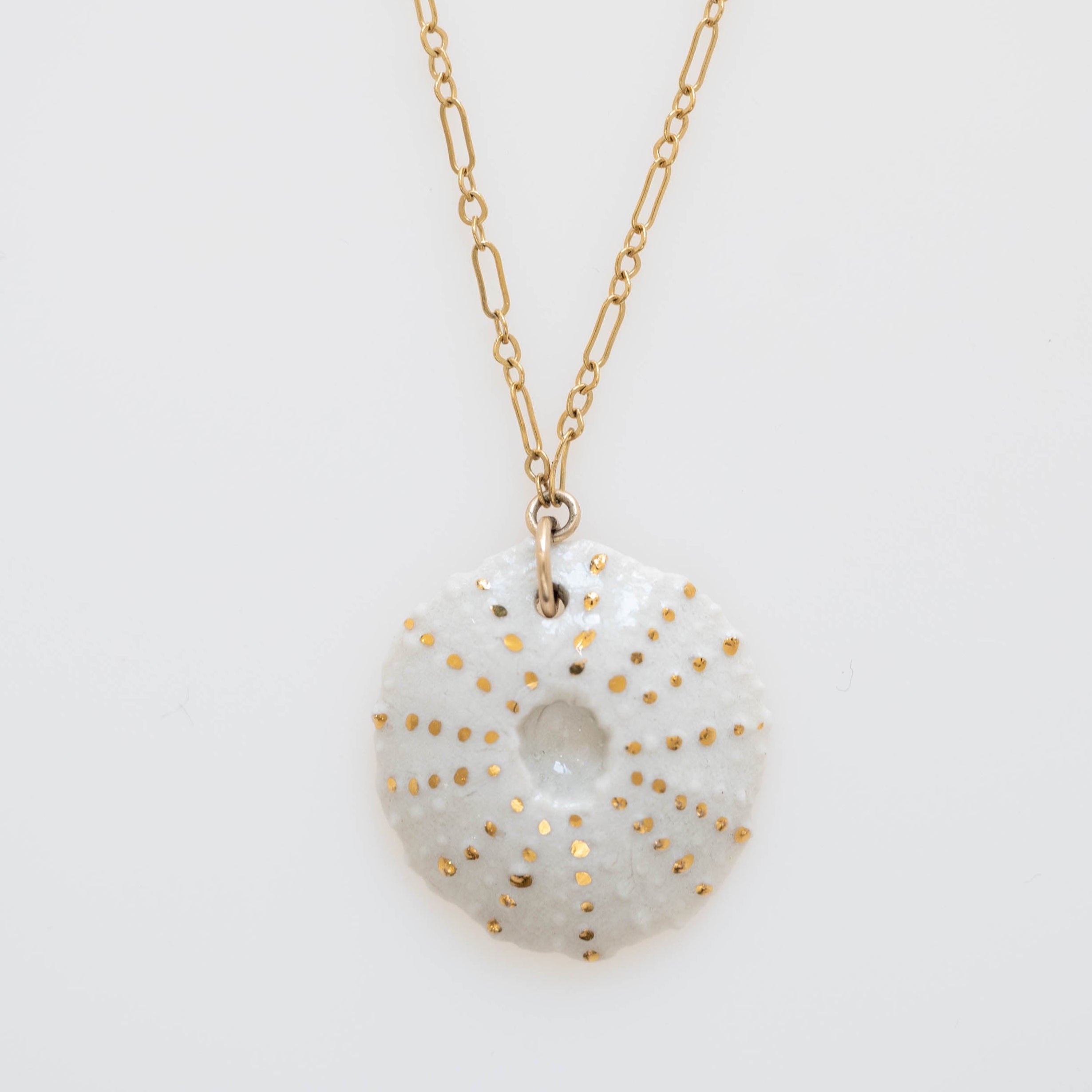 A white porcelain necklace pendant with gold details, resembling a sea anemone, attached to a gold-filled 18" chain.