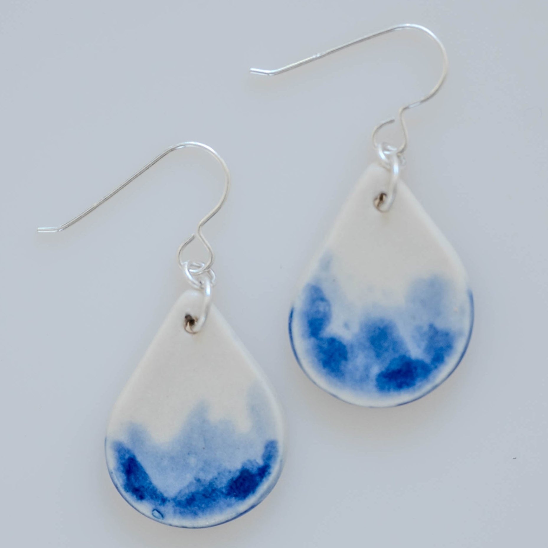 Hand-painted porcelain earrings inspired by rain, featuring blue watercolor design and sterling silver ear wires.