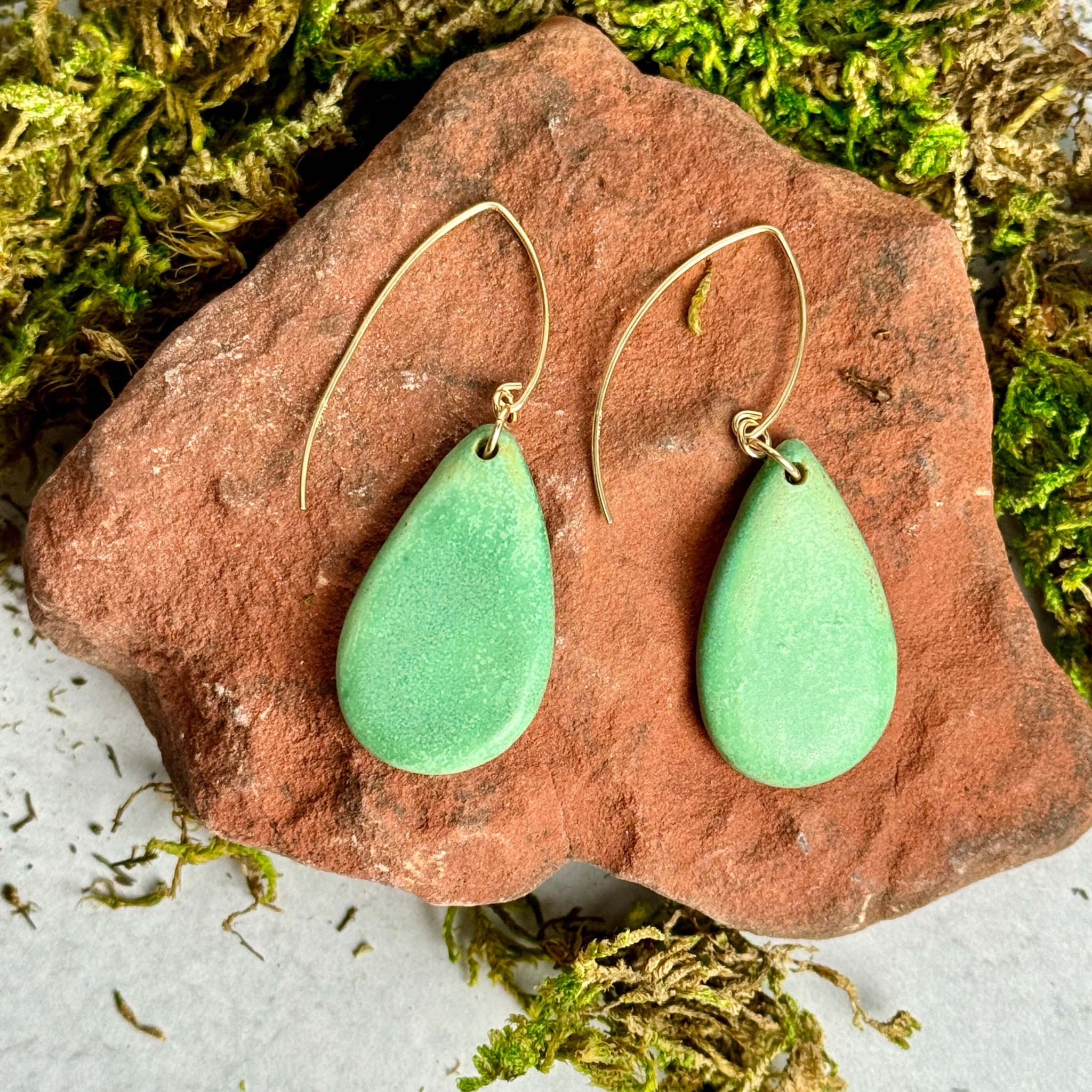 teardrop shaped green earrings resting on on a red rock