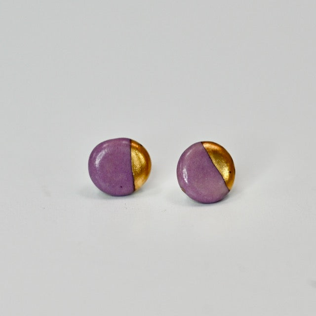 Pair of round earrings with purple and gold half-spheres on a light gray background