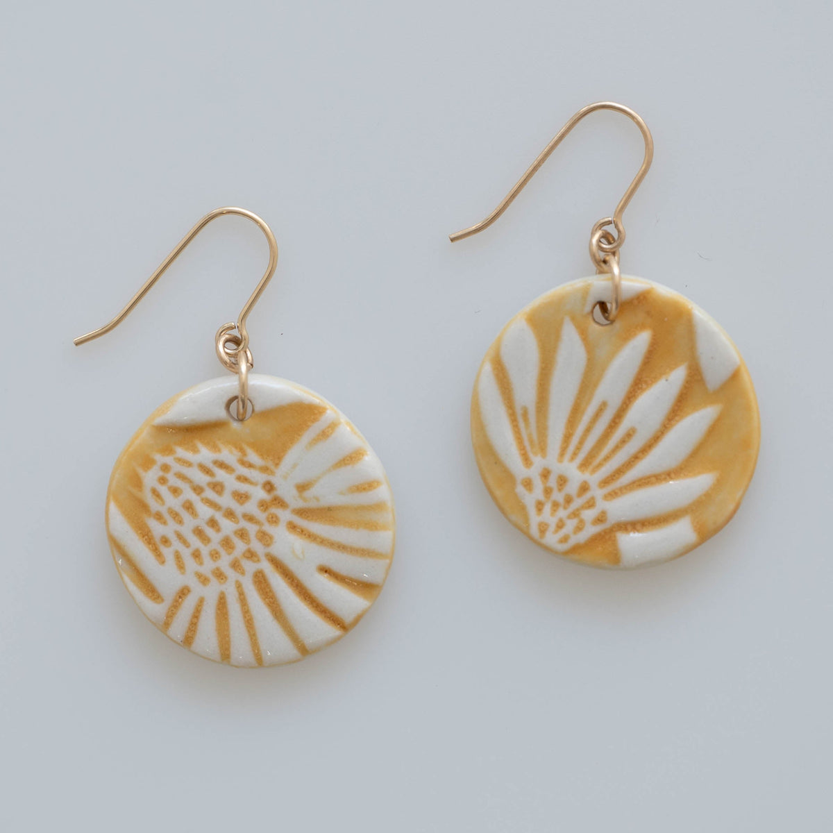 Handmade Sunprint porcelain earrings with raised floral relief, golden ochre glaze and gold-filled ear wires by Hudson Ceramics