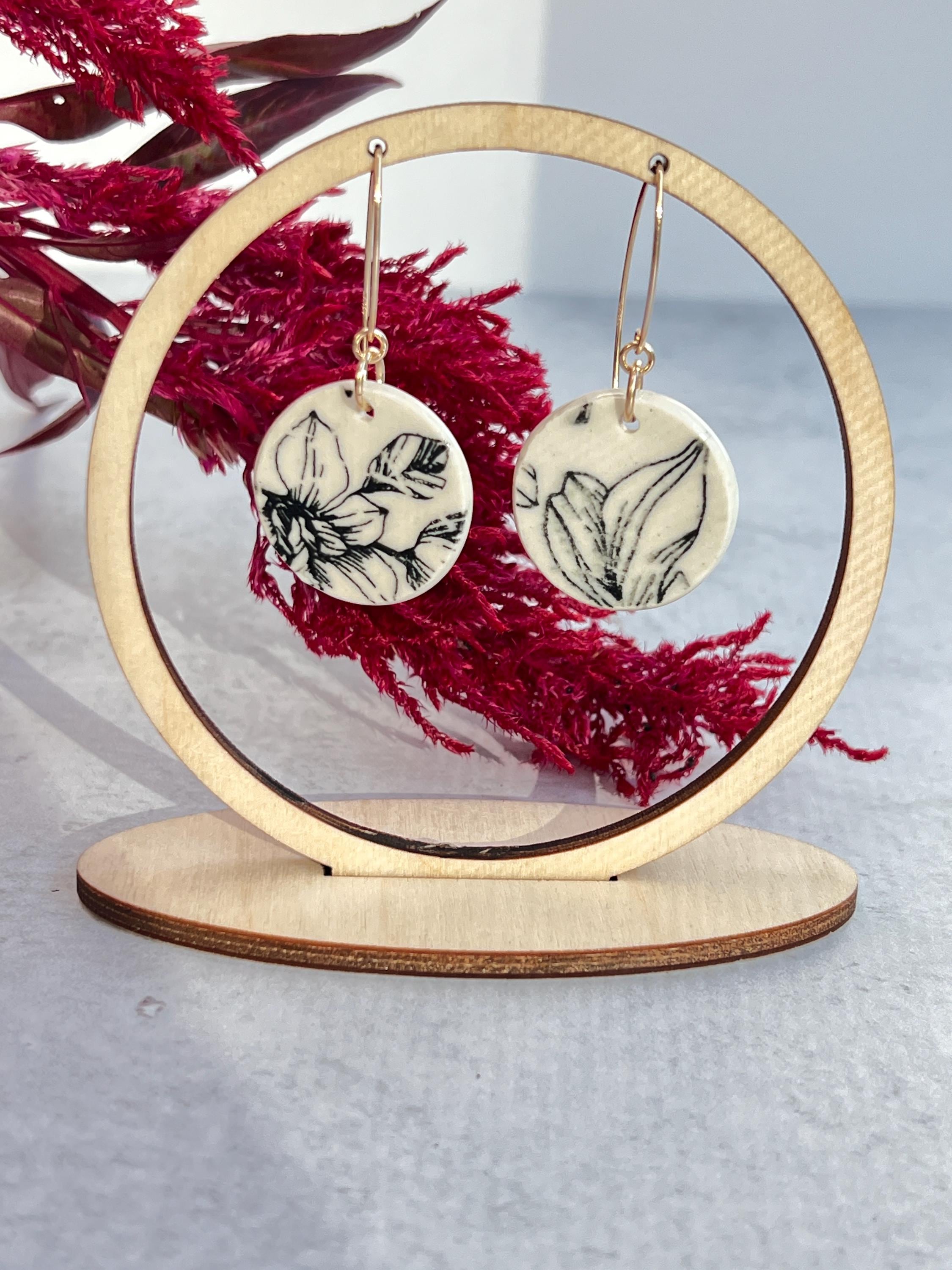 circular floral earrings hanging from circular display with red flower in background