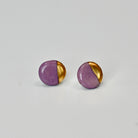 Pair of round earrings with purple and gold half-spheres on a light gray background