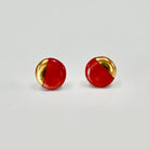 Pair of round earrings with gold and red design on a light gray background