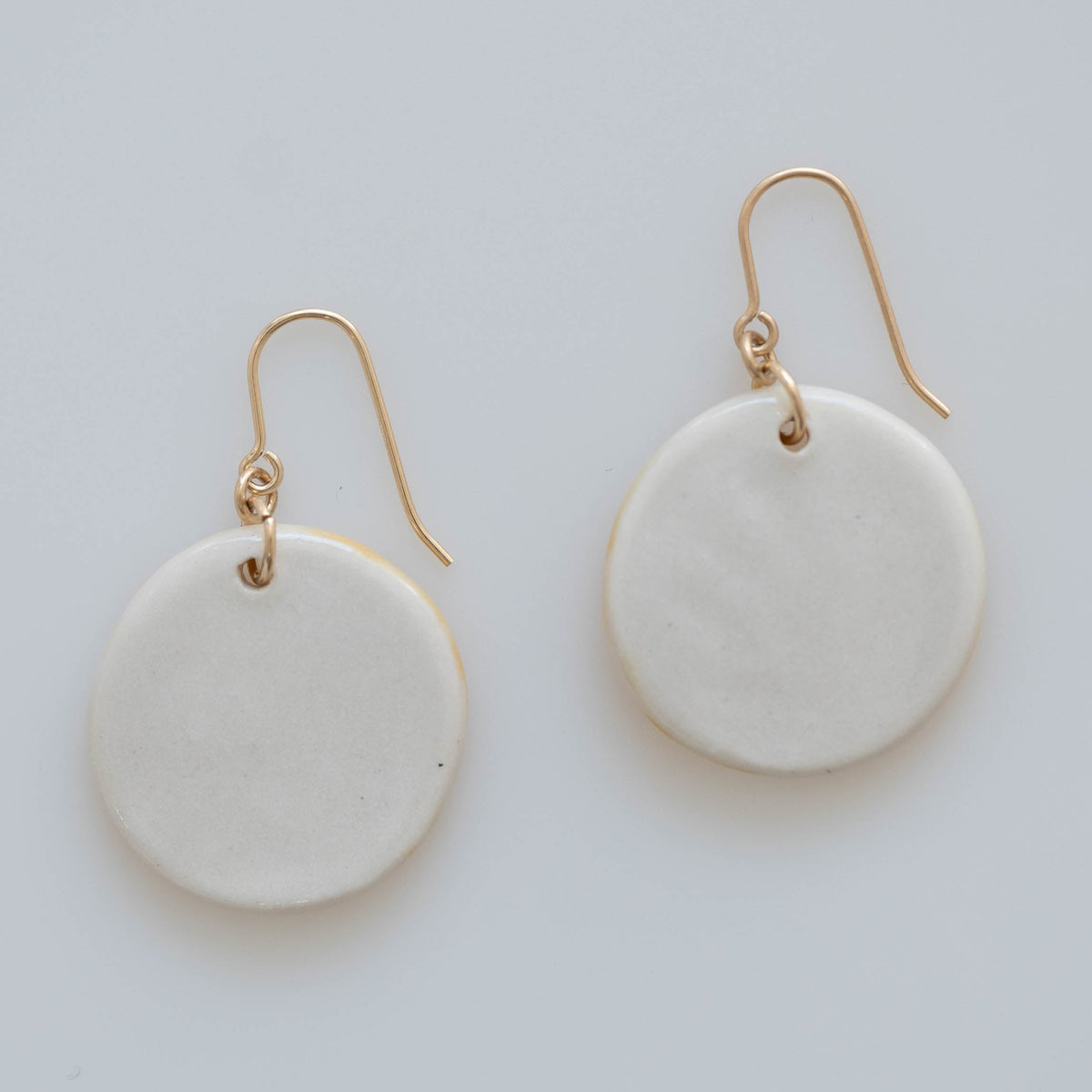 Solid white back view of circular floral earrings with gold ear wires