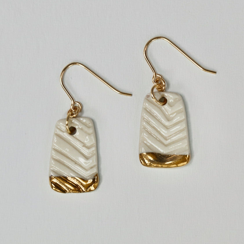Pair of earrings with gold and beige design on a light gray background