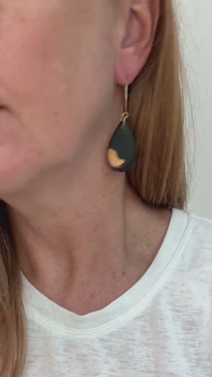 Video of woman wearing teardrop shaped black earrings with gold brushstroke detail and gold ear wires