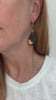 Video of woman wearing teardrop shaped black earrings with gold brushstroke detail and gold ear wires